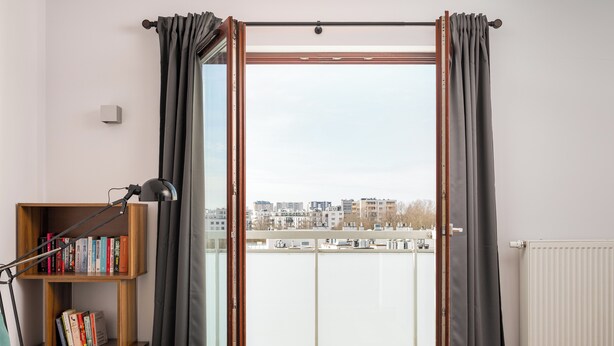 Een moderne woonkamer met een schuifdeur naar een balkon, een boekenkast en een vloerlamp.