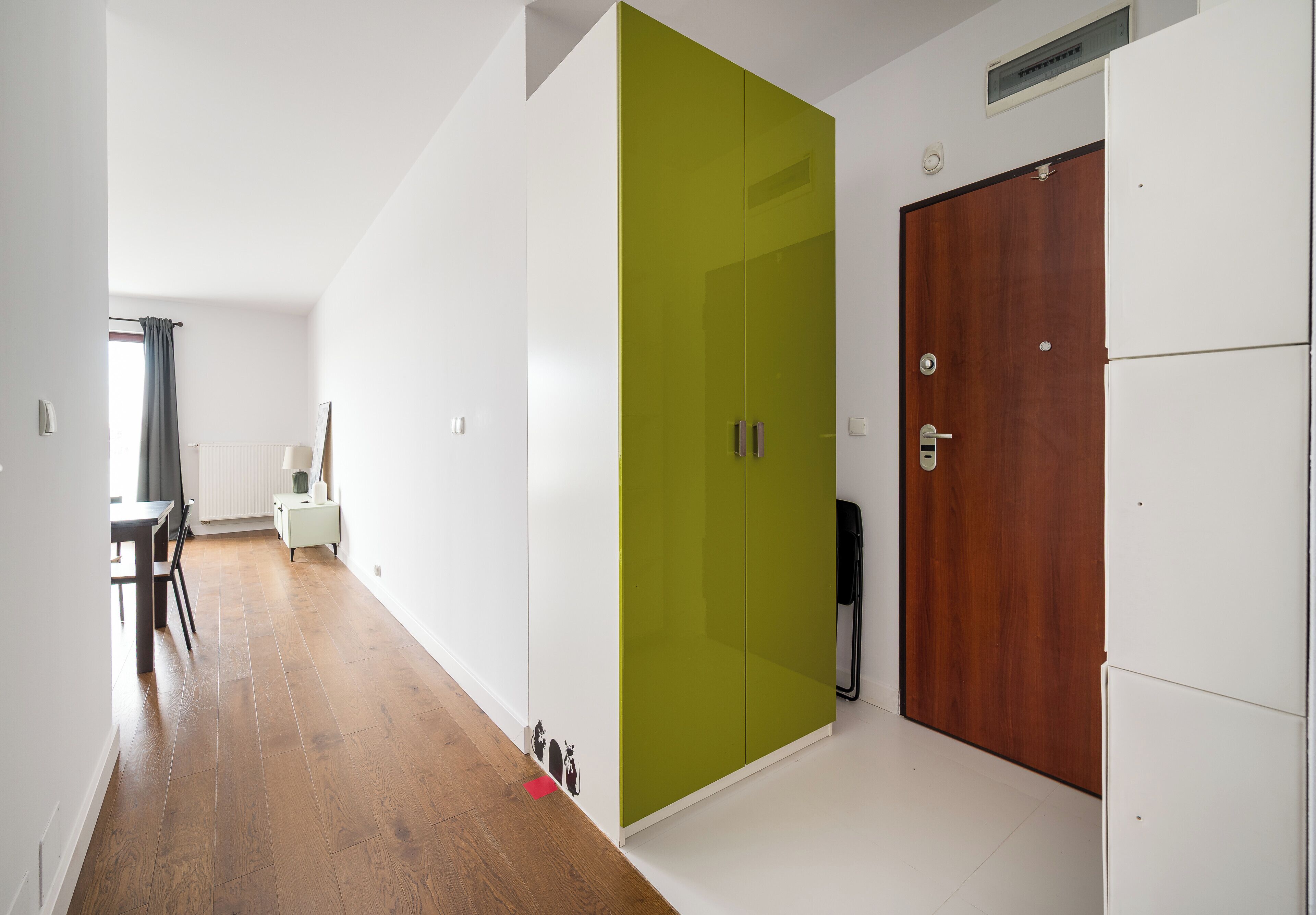 A hallway with a wooden floor, a green wardrobe, a wooden door, and a white refrigerator.