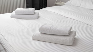 Een opgemaakt bed met witte lakens en twee gevouwen handdoeken.