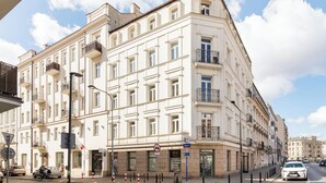 A multi-story building with balconies, a sign for a medical center, and a street with cars and a cyclist. - Park Praski Deluxe Studio (Warszawa)