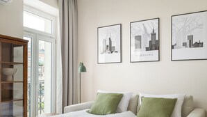A hotel room with a bed, two pillows, a nightstand, a lamp, and three framed cityscape pictures on the wall. - Park Praski Deluxe Studio (Warszawa)