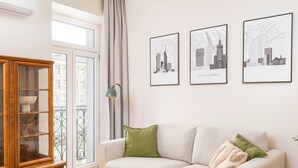 A living room with a sofa, a wooden cabinet, and three framed cityscape pictures on the wall. - Park Praski Deluxe Studio (Warszawa)