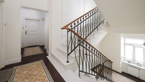 A staircase with a wooden handrail and black metal balusters, leading to a landing with a white door. - Park Praski Deluxe Studio (Warszawa)