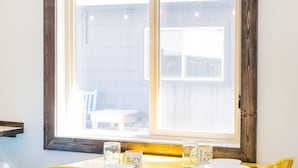 Un coin repas avec une table et des chaises jaunes, une fenêtre donnant sur un beau paysage, et une table dressée avec des assiettes, des verres et des couverts.