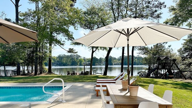 Ein Poolbereich mit Holztisch und -stühlen, einem Pool und Sonnenschirmen.