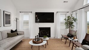 A living room with a fireplace, a sofa, a coffee table, and a TV mounted on the wall. - Serenity House-Water Views, Pet Friendly & Hot Tub (Kill Devil Hills)