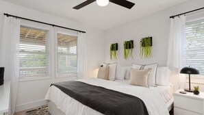 A bedroom with a bed, bedside tables, a ceiling fan, and a window with blinds. - Serenity House-Water Views, Pet Friendly & Hot Tub (Kill Devil Hills)