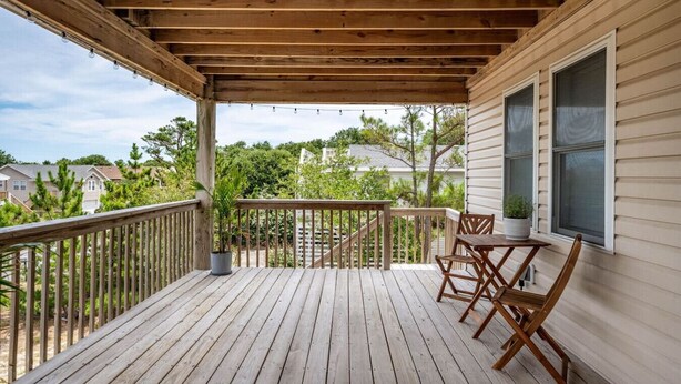 A wooden deck with a railing, a table, and chairs. - Serenity House-Water Views, Pet Friendly & Hot Tub (Kill Devil Hills)