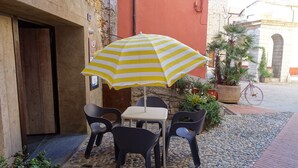 An outdoor seating area with a striped umbrella, stone tiles, and potted plants.