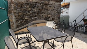 Een terras met een stenen muur, een metalen tafel en stoelen, en een overdekt gedeelte.