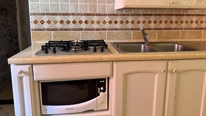 Een keuken met een gasfornuis, een magnetron, een spoelbak en een betegelde spatwand.