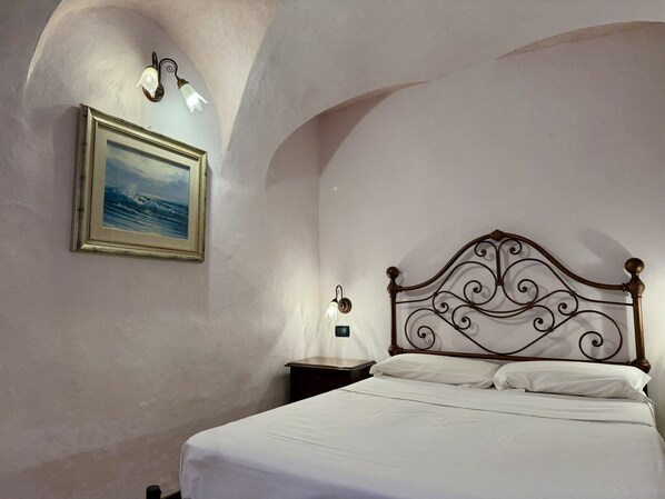 A bedroom with a bed, a nightstand, a wall-mounted light, and a framed picture.