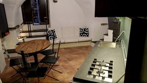A compact kitchen with a gas stove, a dining table with chairs, and a small seating area with a bench and decorative pillows.