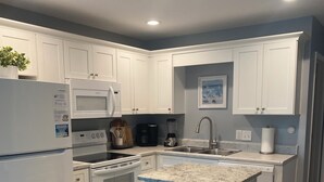 Moderni keittiö, jossa on valkoiset kaapit, sisäänrakennettu uuni, mikroaaltouuni ja jääkaappi.