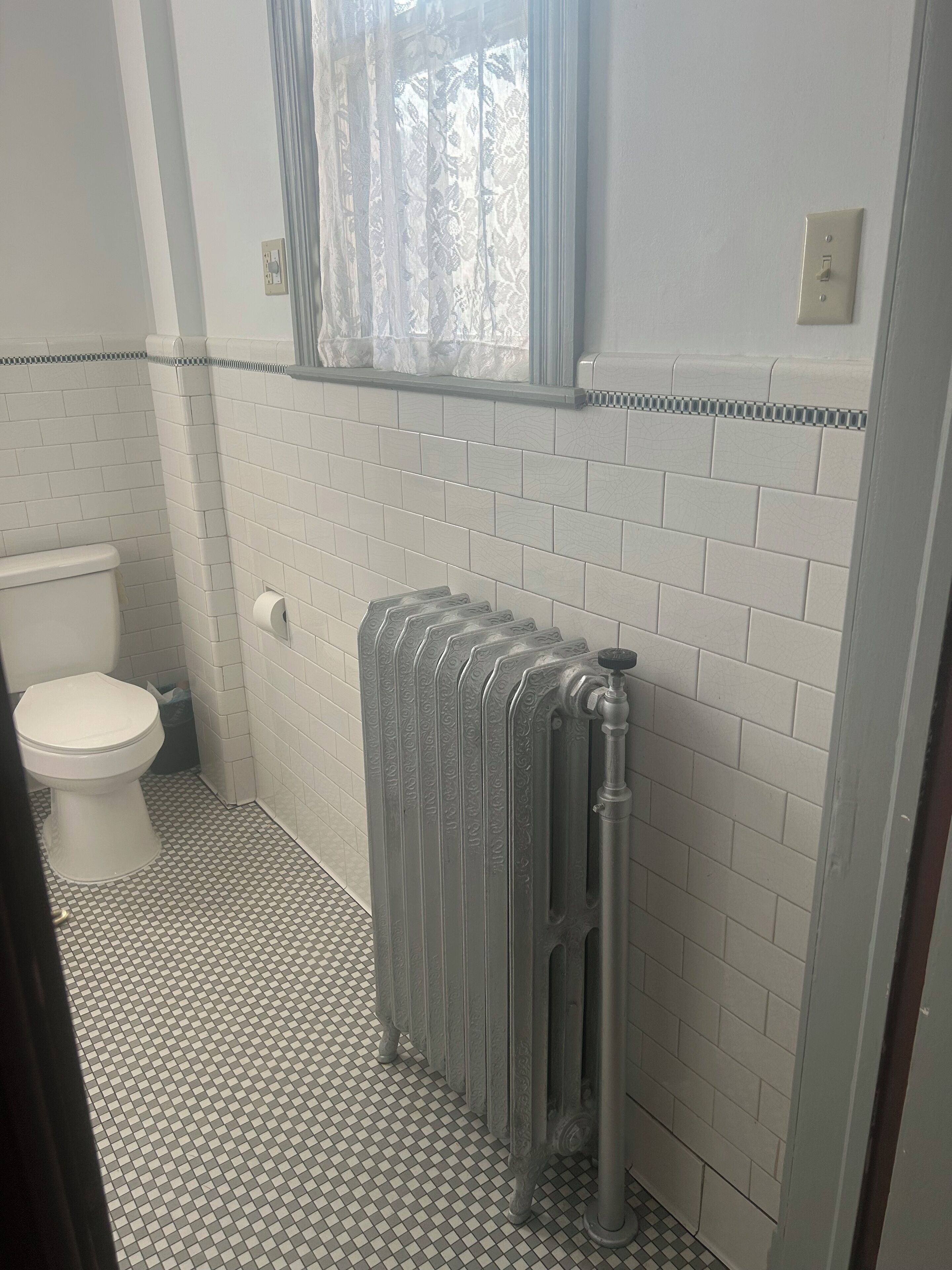 A bathroom with a toilet, a radiator, and patterned floor tiles.