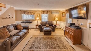 A living room with a brown leather sofa, a brown leather armchair, a matching ottoman, a wooden cabinet, and a flat-screen TV mounted on the wall.
