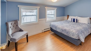 A bedroom with two windows, a bed with patterned bedding, a chair, and a ceiling light fixture.