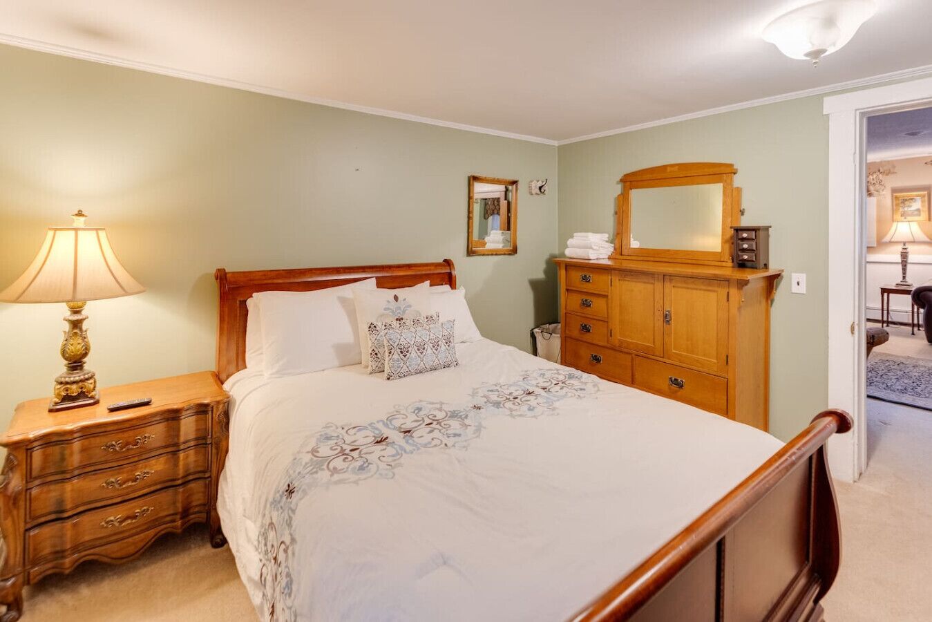 A neatly arranged bedroom with a wooden bed, a nightstand with a lamp, a dresser, and a mirror.