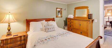 A neatly arranged bedroom with a wooden bed, a nightstand with a lamp, a dresser, and a mirror.