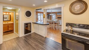 A modern kitchen with a built-in oven, a dining area with a wooden table, and a round clock on the wall.