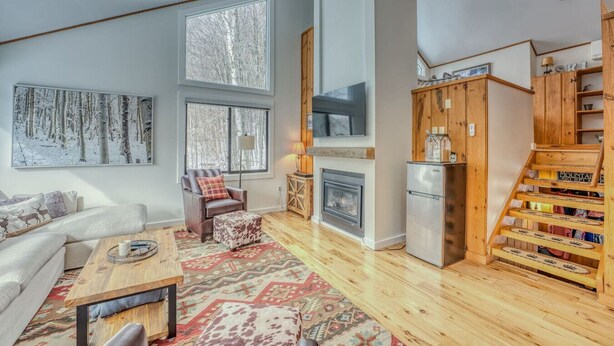 Ein großzügiges Wohnzimmer mit Kamin, einer Couch, einem Couchtisch und einem großen Fenster mit Blick auf Bäume.