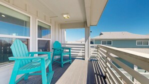 A balcony with turquoise Adirondack chairs, a white railing, and a view of a house across the water. - PPLM401 Private Heated Pool, Golf Cart Included, Close to the Beach (Port Aransas)