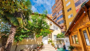 A residential building with a wooden facade, a staircase leading to a door, and a small garden area with potted plants. - Guesthouse 'hapa të Lehtë' - Room 1 - Pro Bono (Shkodër)