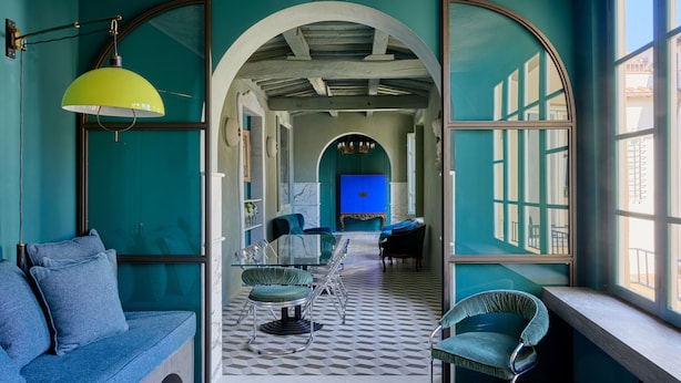 A room with a checkered floor, a blue sofa, and a dining area with chairs and a table. - Bella Vista Duomo - Luxury Apartment in Lucca (Lucca)
