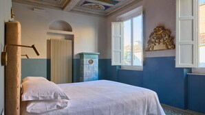A bedroom with a bed, a radiator, a window with white shutters, and a decorative ceiling. - Bella Vista Duomo - Luxury Apartment in Lucca (Lucca)