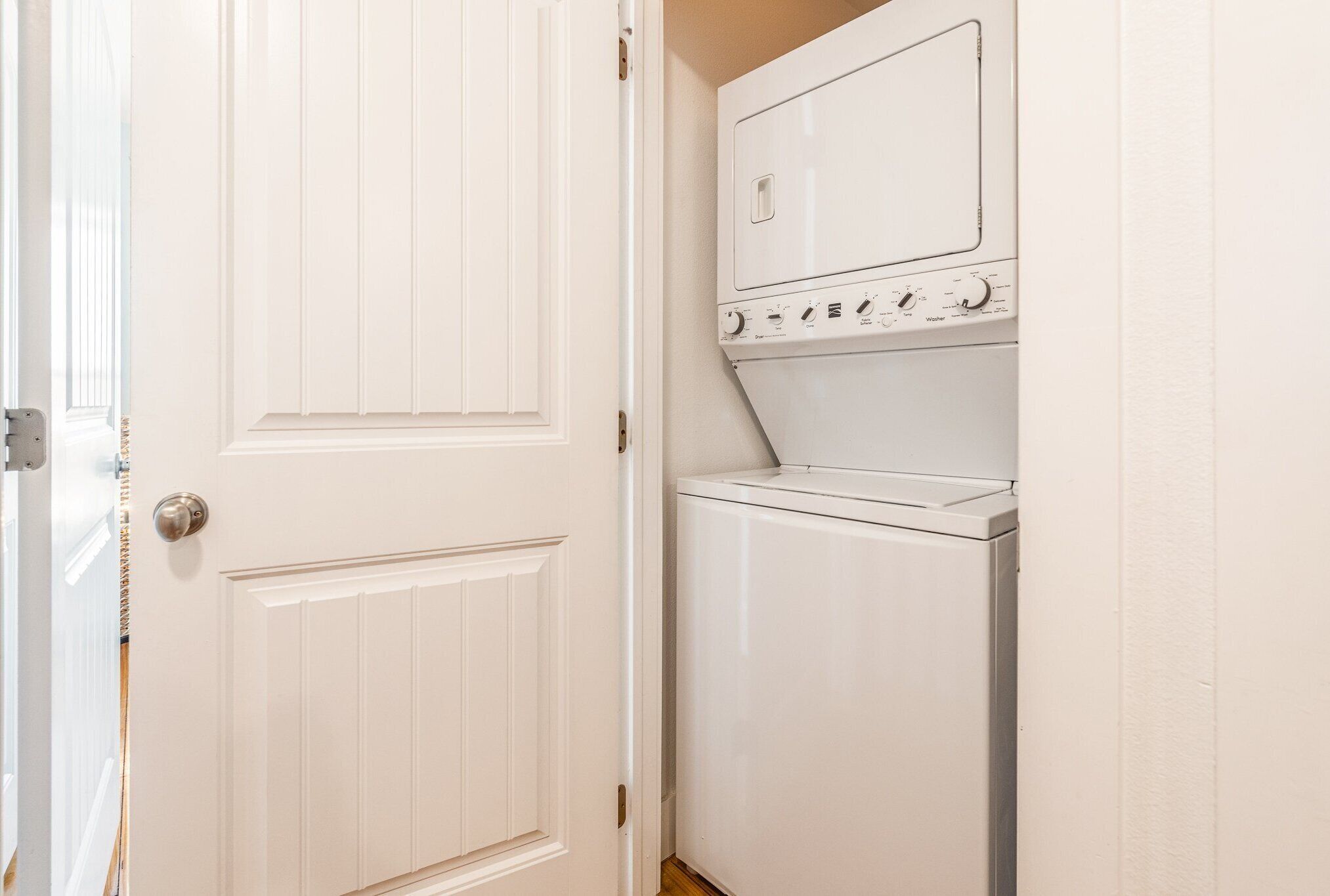 A laundry room with a white door and a stacked washer and dryer.