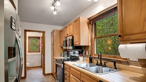 Eine moderne Küche mit Holzschränken, Edelstahlgeräten und einem großen Fenster mit Blick auf Grünflächen.