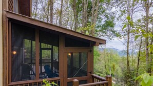 Eine Holzterrasse mit Glasumrandung, umgeben von Bäumen und einer Bergkulisse.