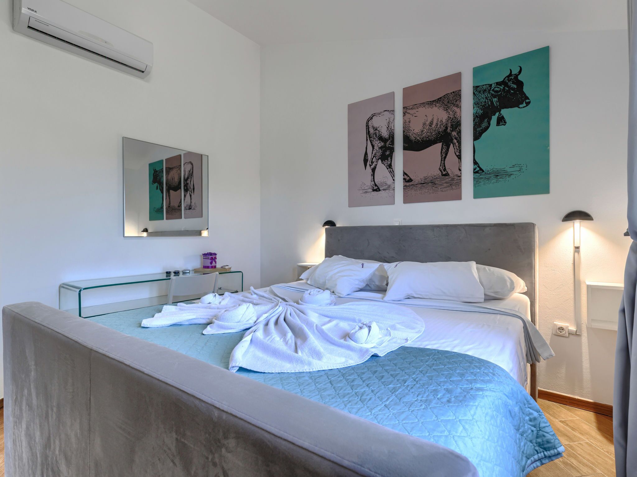 A hotel room with a bed, a bedside table, a mirror, and artwork on the wall.