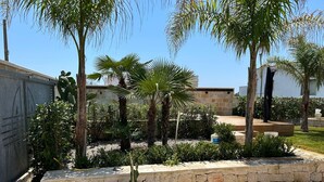 A courtyard with palm trees, a stone wall, and a potted plant. - Villa Romolo with swimming pool 150 mt from the Caribbean beach of San Pietro (San Pietro In Bevagna)