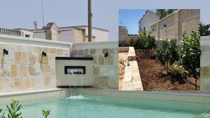 Ein Swimmingpool mit Wasserfall, umgeben von Steinmauern und Grünpflanzen.