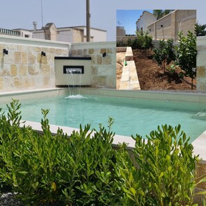 Une piscine agrémentée d’une cascade, entourée de murs de pierre et de verdure.