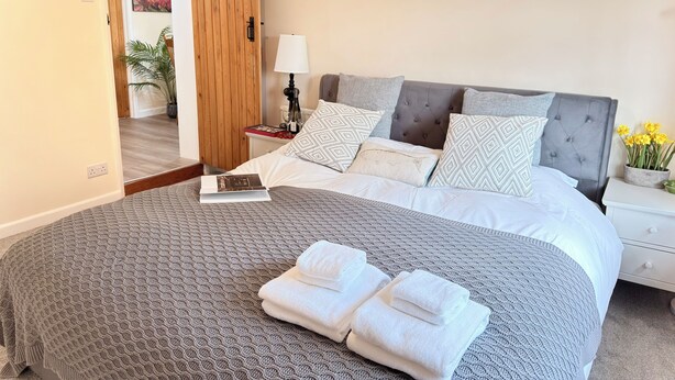 A neatly made bed with a patterned blanket, a bedside table with a lamp, and a nightstand with a vase of flowers.