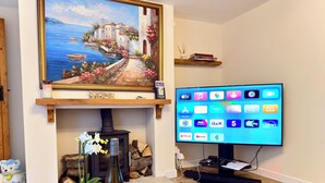 A living room with a painting of a coastal scene, a television displaying app icons, a bottle of wine, and a Monopoly board game.