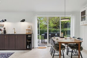 A modern kitchen with a dining area, large windows, and a view of greenery.