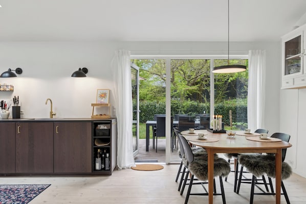 A modern kitchen with a dining area, large windows, and a view of greenery.