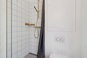 Ein Badezimmer mit weißen Fliesen, einer Dusche mit goldfarbener Duschbrause und einer weißen Toilette.