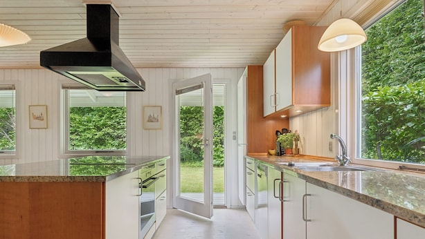 A modern kitchen with a large island, wooden cabinets, and a view of greenery outside.