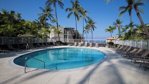 Zona de piscina con sillones de descanso, palmeras y un edificio de fachada de piedra.