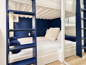 A bunk bed with a white mattress and blue headboard, a white pillow, and a blue blanket.