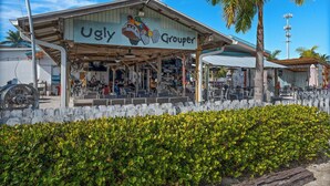 A building named 'Ugly Grouper' with outdoor seating and a palm tree in the foreground.