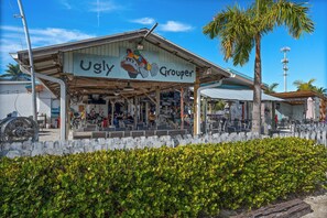 Un edificio llamado 'Ugly Grouper' con mesas al aire libre y una palmera en primer plano.