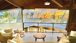 A room with wicker furniture, large windows, and a view of a building and palm trees. - One Of The Most Unique Homes in Anna Maria Island (Holmes Beach)