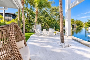 An outdoor patio with white lounge chairs, a wicker sofa, and a poolside area with a view of the water.