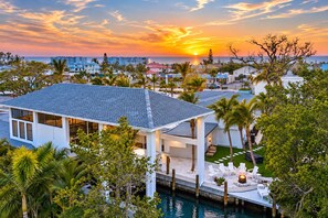 A modern house with a pool, surrounded by palm trees and a sunset view.