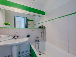 Ein Badezimmer mit weißem Waschbecken, einem spiegel mit grünem Streifenmuster und einer Badewanne.
